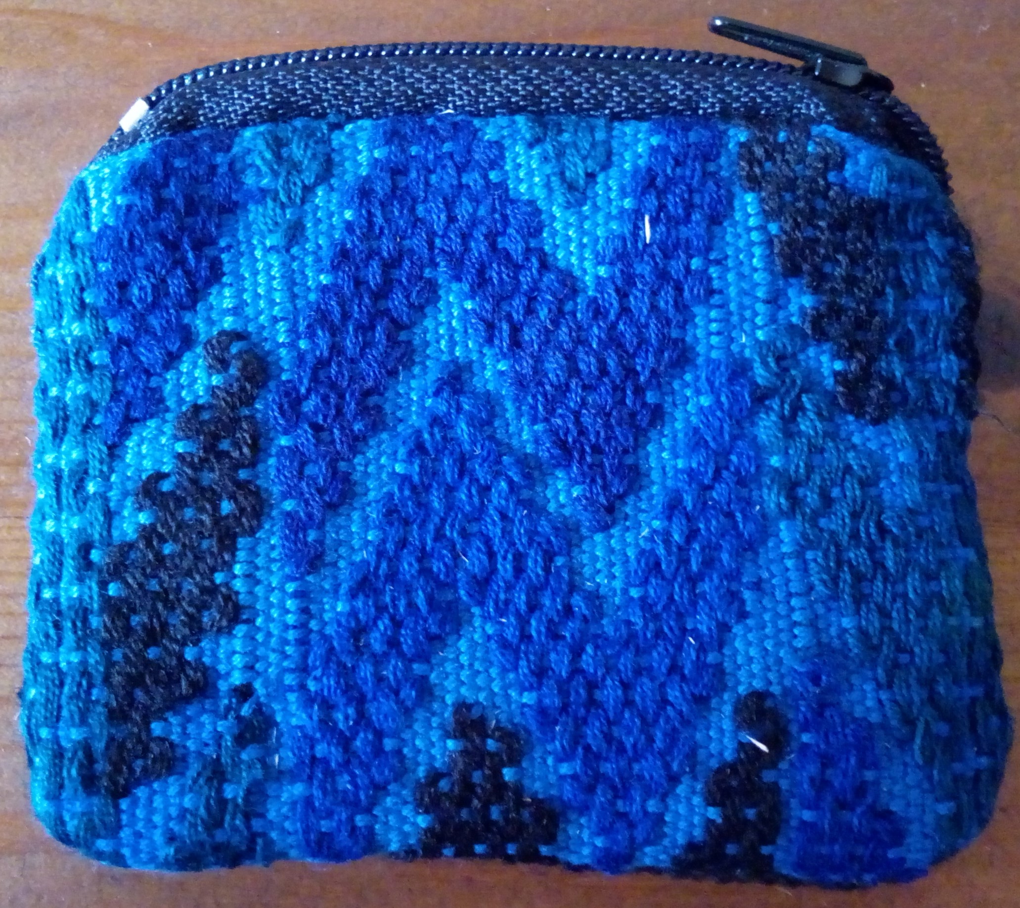 Υφασμάτινo πορτοφόλι MAYA με μοναδική χειροποίητη πλέξη στο μπροστινό τμήμα. Το πίσω τμήμα είναι μαύρο ύφασμα. Μία θήκη. Διαστάσεις: 8.5cm x 7cm.